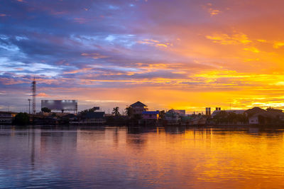 Scenic view of river by buildings against sky during sunset