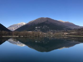 Scenic view of lake and mountains against clear blue sky