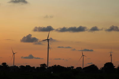 Silhouette wind turbines on field against sky during sunset