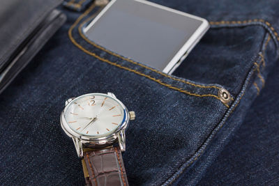 Close-up of watch and mobile phone on denim jeans