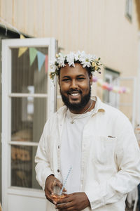 Portrait of smiling young man wearing tiara while holding wineglass during dinner party at cafe