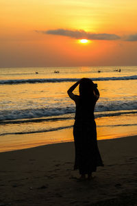 Rear view of silhouette woman standing on beach during sunset