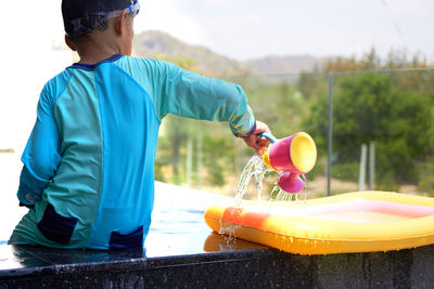 Rear view of boy holding water pot on poolside 