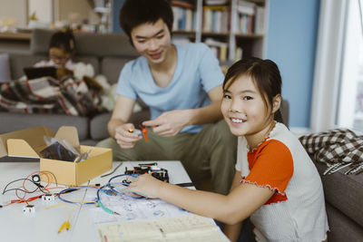 Smiling portrait of girl making science project sitting with brother at home