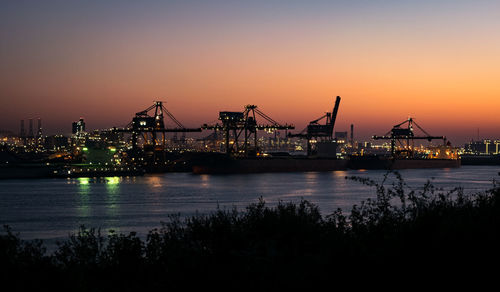 Illuminated pier at harbor against sky during sunset