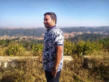 Side view of young man standing on landscape against clear sky