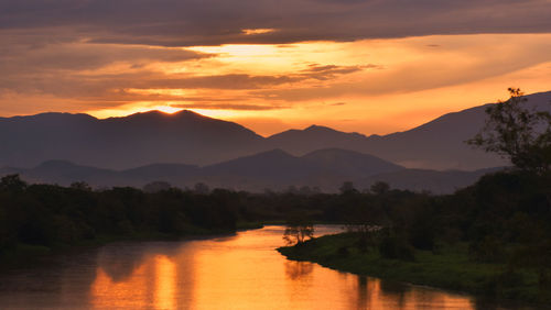 Scenic view of river by silhouette mountains against orange sky