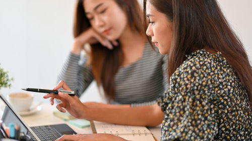 College students, female college student using tablet for teaching math homework to her classmate 