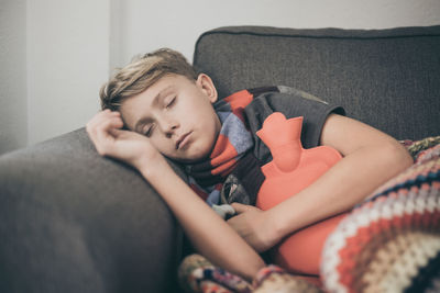 Ill boy sleeping with hot water bottle on sofa