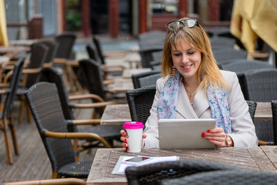 Woman using digital tablet while sitting at sidewalk cafe in city