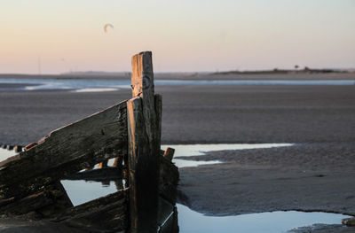 Wooden post on beach against sky during sunset