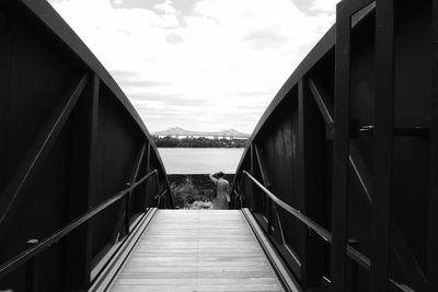 Woman standing on footbridge against sky