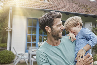 Happy father carrying son in front of their home