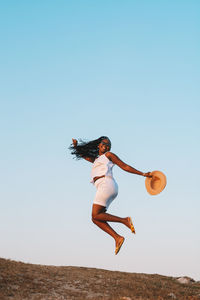 Low angle view of woman jumping against clear sky
