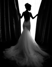 Rear view of fashion model in wedding dress while holding curtains