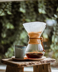 Close-up of coffee in container with mug on table against plants