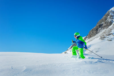 Rear view of man skiing on snow covered mountain against clear blue sky