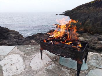 Bonfire on rocks by sea against sky