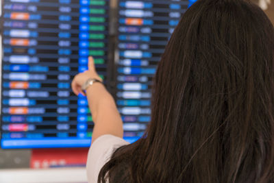 Rear view of woman pointing at arrival departure board