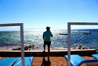 Rear view of man standing against clear blue sky at beach