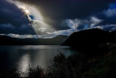 Scenic view of lake and mountains against storm clouds