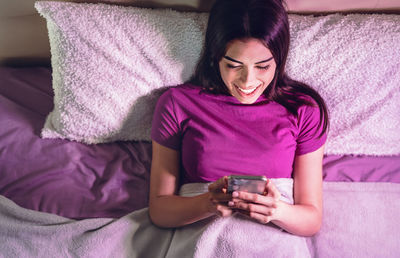 Midsection of woman using mobile phone while relaxing on bed at home