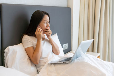 Young woman sitting on bed at home