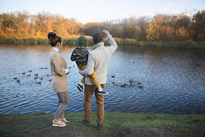 Rear view of friends standing by lake against trees