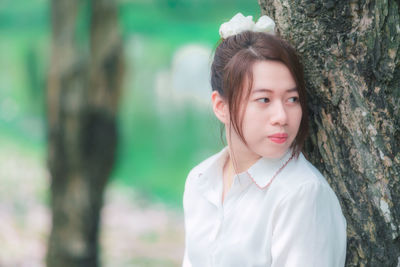 Portrait of woman against tree trunk in forest