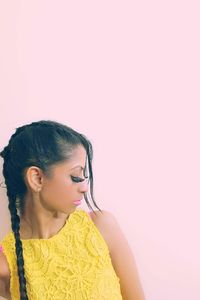 Close-up of young woman standing against pink background