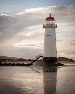 Lighthouse by sea against sky during sunset