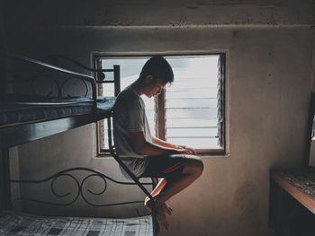 Side view of young man sitting on ladder of bunkbed