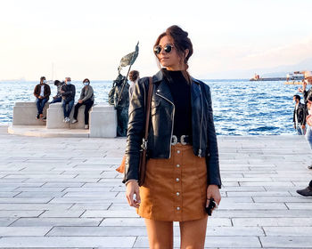 Young woman standing on sea shore against sky