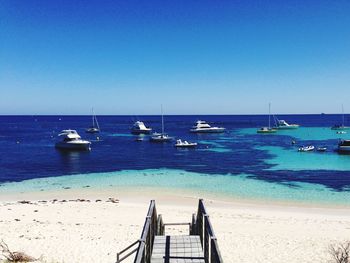 Sailboats moored on sea against clear blue sky