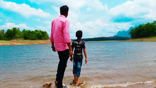 Rear view of men walking on shore against sky