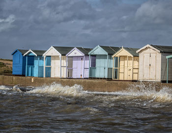 Beach huts in row by sea against cloudy sky