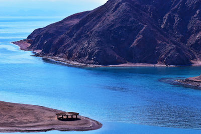 Scenic view of sea against blue sky, mountains and a lonely hut