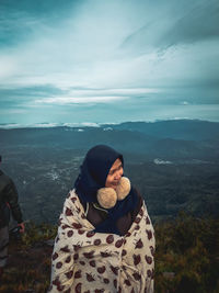 Woman wrapped in blanket looking away while standing against mountains