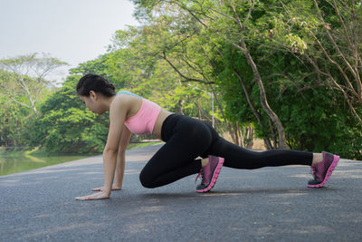 Full length of young woman exercising on road by river at park
