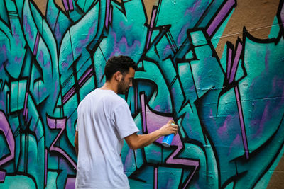 Side view of young man standing against graffiti wall