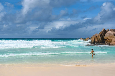 Rear view of woman standing alone on tropical sandy beach with idyllic turquoise ocean