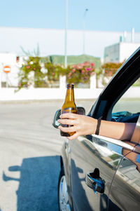Man holding glass bottle against road in city