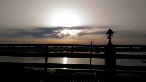 Silhouette bridge over sea against sky during sunset