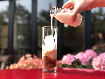Cropped hand pouring milk in iced coffee on table