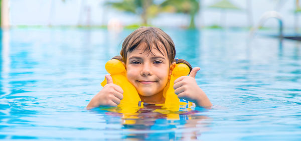 Girl in life jacket gesturing thumbs in swimming pool