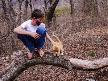Teenage boy with cat crouching on fallen tree