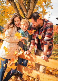 Cheerful family standing by wooden railing during autumn in park
