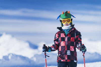 Portrait of boy standing while skiing on land against mountains and sky