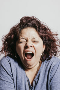 Close-up of mid adult woman yawning against white background