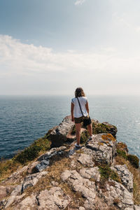 Rear view of woman standing on rock against sky